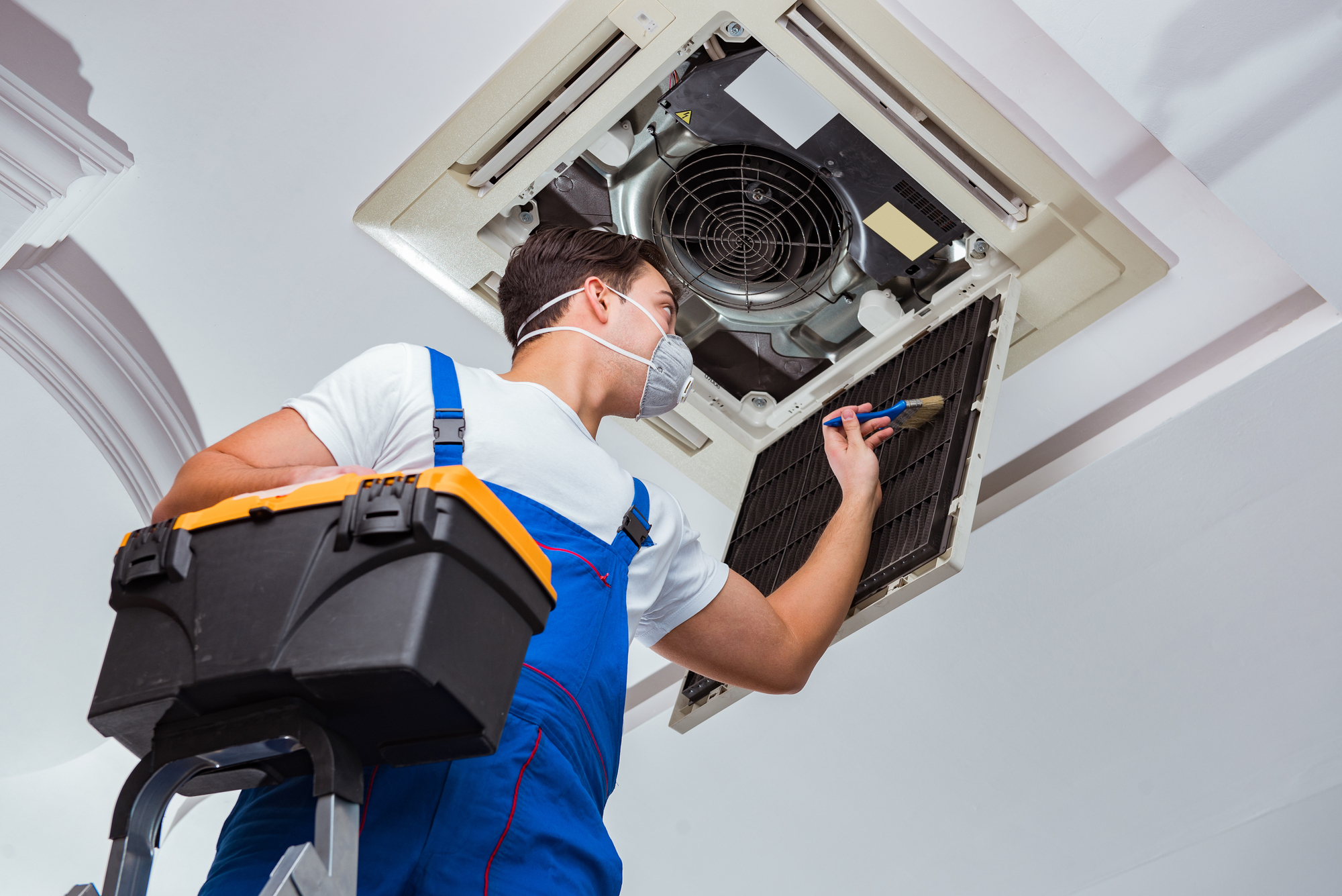 A Man in Blue Overalls Fixing an Air Conditioner.