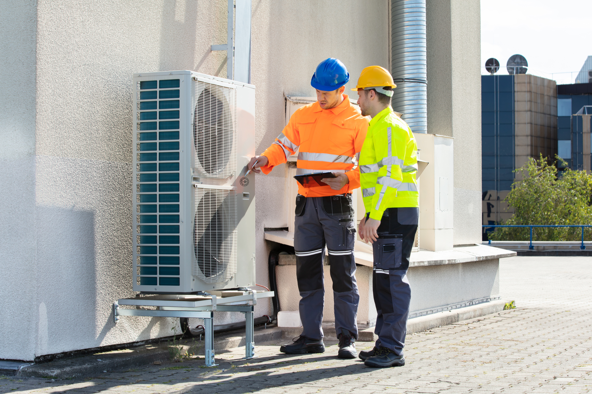 Two Workers in Safety Gear by an Air Conditioner.